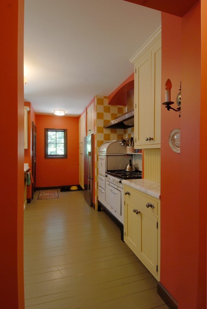 Eklektisk inredning av ett avskilt, mellanstort l-kök, med en undermonterad diskho, skåp i shakerstil, gula skåp, marmorbänkskiva, gult stänkskydd, stänkskydd i trä, rostfria vitvaror, målat trägolv, en halv köksö och beiget golv
