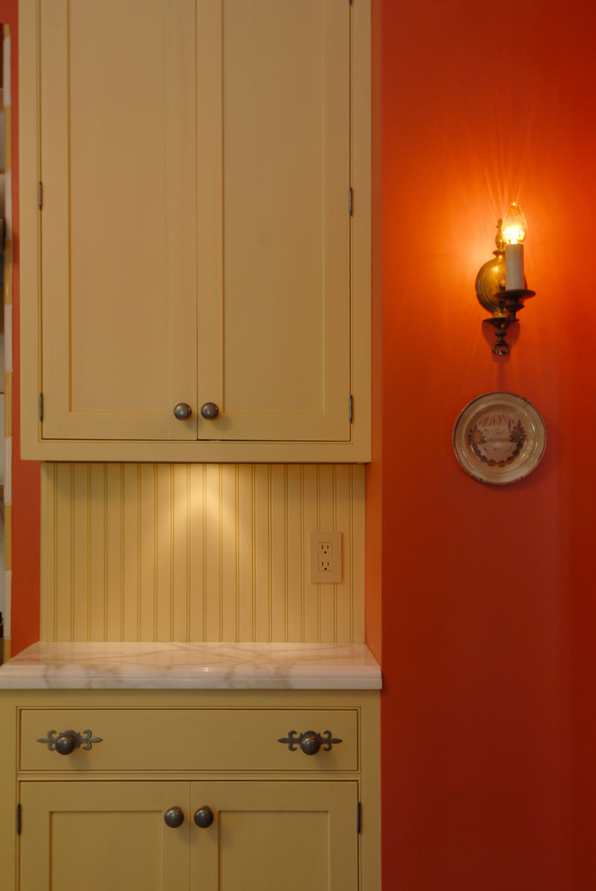 サンフランシスコにある高級な中くらいなエクレクティックスタイルのおしゃれなキッチン (アンダーカウンターシンク、シェーカースタイル扉のキャビネット、黄色いキャビネット、大理石カウンター、黄色いキッチンパネル、木材のキッチンパネル、シルバーの調理設備、塗装フローリング、ベージュの床) の写真