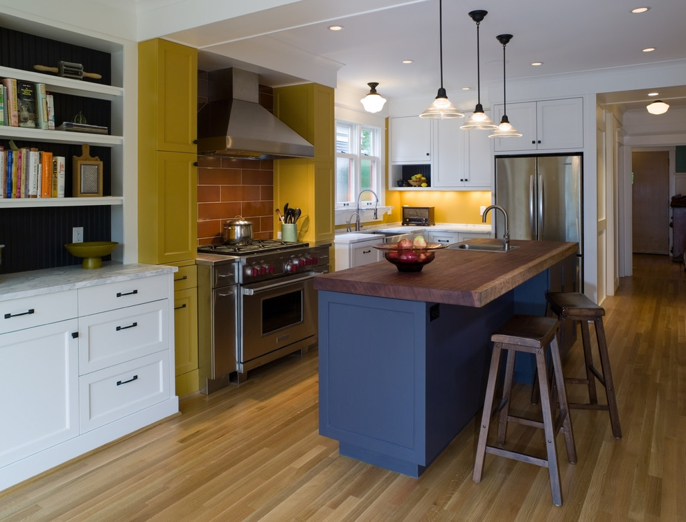Imagen de cocina contemporánea con electrodomésticos de acero inoxidable, encimera de madera, armarios estilo shaker, puertas de armario amarillas, suelo marrón y encimeras marrones