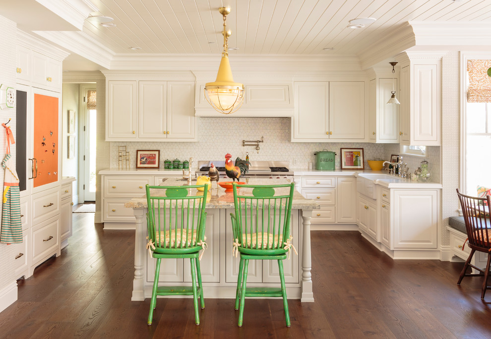 Inspiration for a classic u-shaped kitchen/diner in Los Angeles with a belfast sink, raised-panel cabinets, white cabinets, white splashback, ceramic splashback, integrated appliances, medium hardwood flooring and an island.