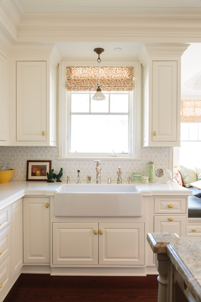 Elegant medium tone wood floor kitchen photo in Los Angeles with a farmhouse sink, recessed-panel cabinets, white cabinets, white backsplash, ceramic backsplash and an island