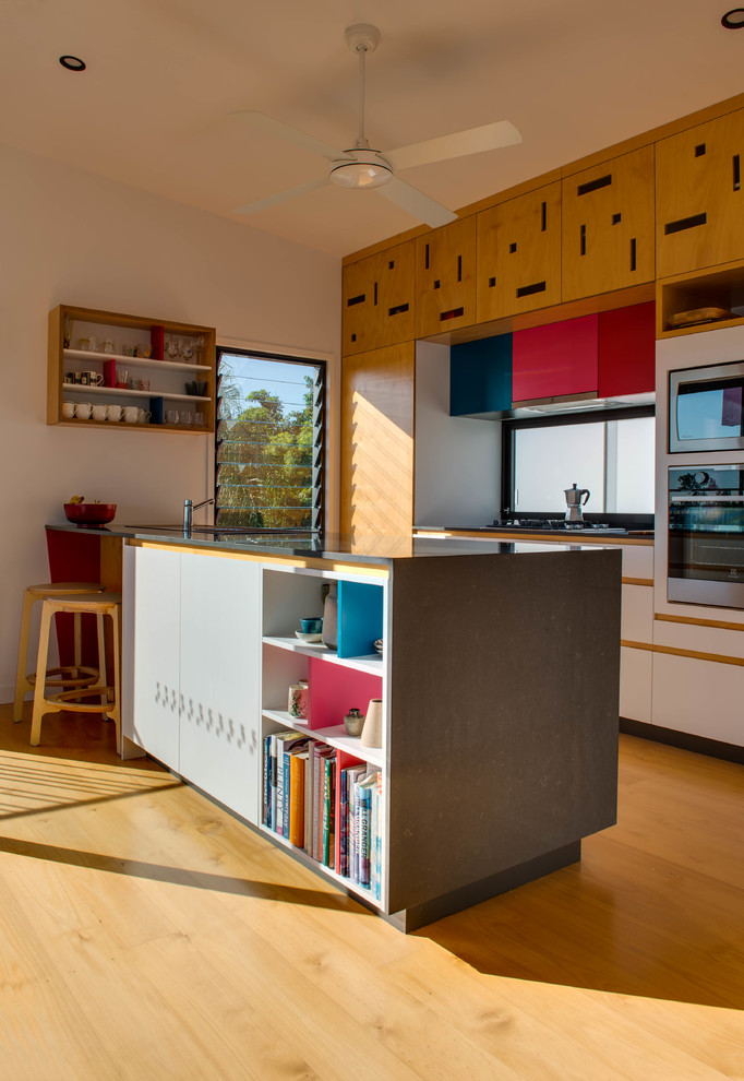 Cette image montre une cuisine ouverte parallèle design en bois clair de taille moyenne avec fenêtre, un électroménager noir, parquet clair et îlot.
