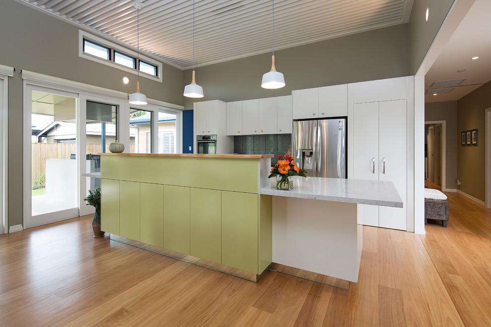 Foto på ett mellanstort funkis kök, med en nedsänkt diskho, släta luckor, vita skåp, bänkskiva i kvarts, grönt stänkskydd, stänkskydd i glaskakel, rostfria vitvaror, mellanmörkt trägolv och en köksö