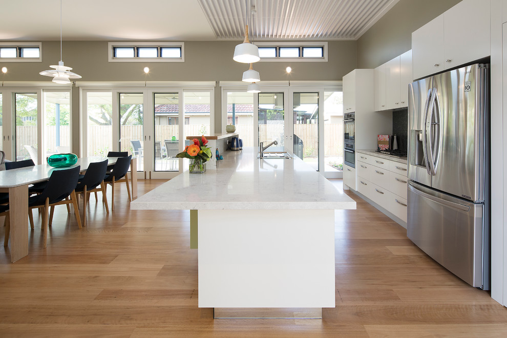 Design ideas for a medium sized contemporary galley kitchen/diner in Brisbane with a built-in sink, flat-panel cabinets, white cabinets, engineered stone countertops, green splashback, glass tiled splashback, stainless steel appliances, medium hardwood flooring and an island.