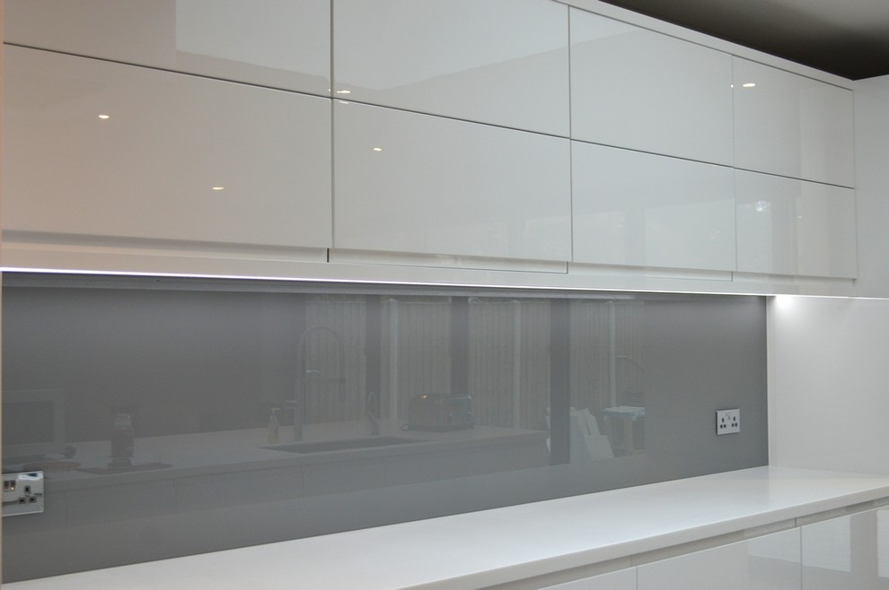Modern kitchen in Hertfordshire with grey splashback and glass sheet splashback.