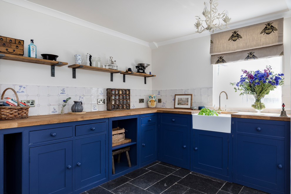 ロンドンにある高級な広いカントリー風のおしゃれなキッチン (エプロンフロントシンク、シェーカースタイル扉のキャビネット、青いキャビネット、木材カウンター、白いキッチンパネル、セラミックタイルのキッチンパネル、パネルと同色の調理設備、ライムストーンの床、アイランドなし、青い床) の写真