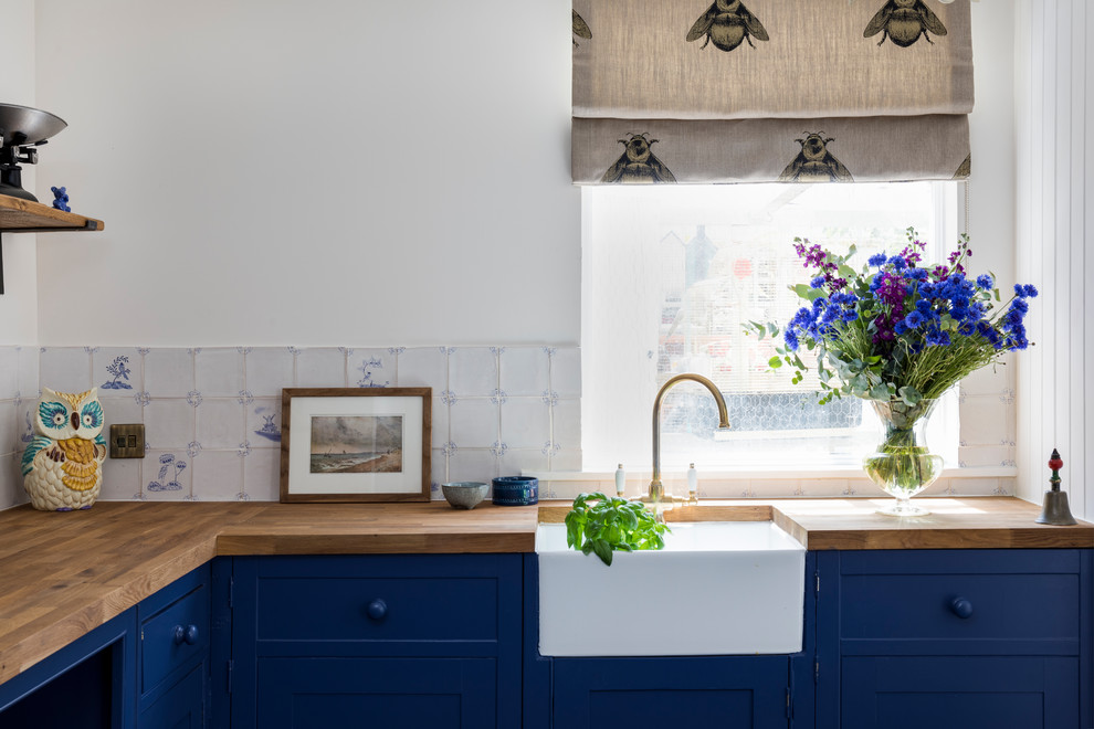 Bild på ett stort lantligt kök, med en rustik diskho, skåp i shakerstil, blå skåp, träbänkskiva, vitt stänkskydd, stänkskydd i keramik, integrerade vitvaror, kalkstensgolv och blått golv