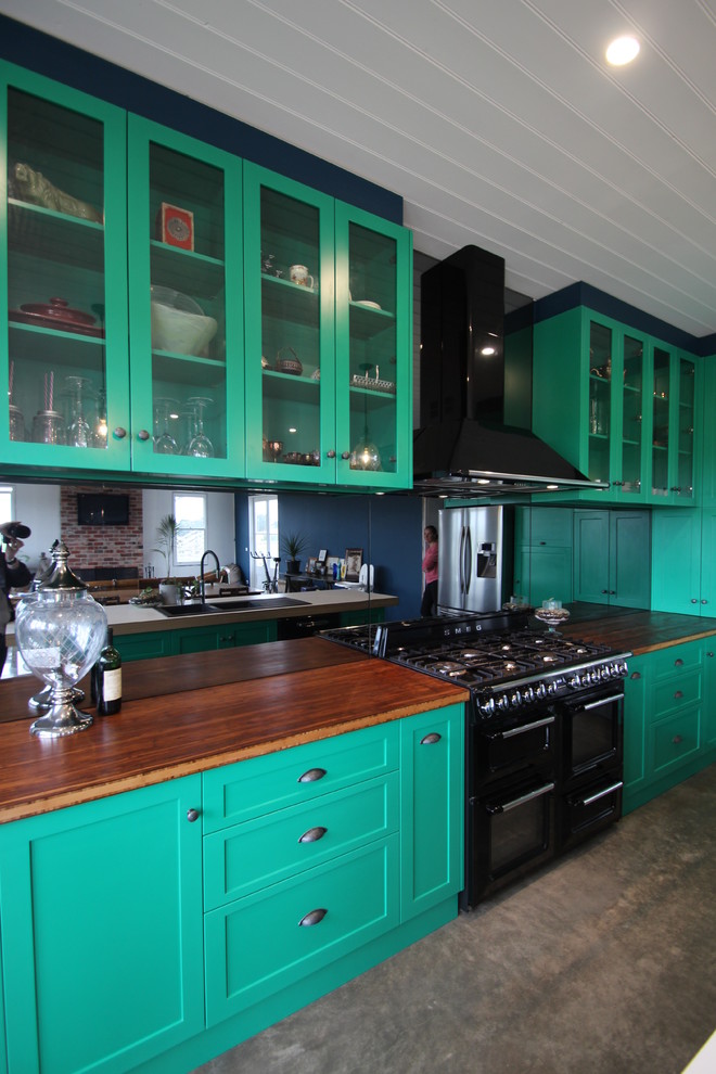 Inspiration for a large eclectic l-shaped kitchen/diner in Melbourne with a belfast sink, shaker cabinets, green cabinets, wood worktops, metallic splashback, mirror splashback, black appliances, concrete flooring and an island.