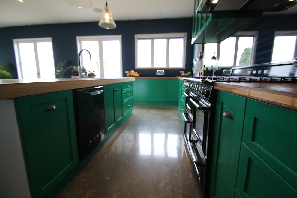 Eklektisk inredning av ett stort kök, med en rustik diskho, skåp i shakerstil, gröna skåp, träbänkskiva, stänkskydd med metallisk yta, spegel som stänkskydd, svarta vitvaror, betonggolv och en köksö