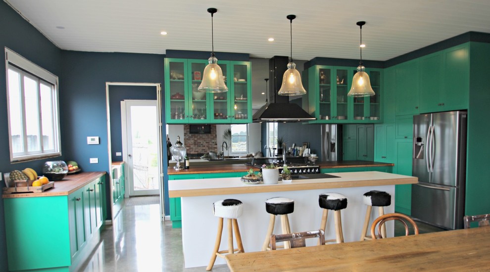 Bild på ett stort eklektiskt kök, med en rustik diskho, skåp i shakerstil, gröna skåp, träbänkskiva, stänkskydd med metallisk yta, spegel som stänkskydd, svarta vitvaror, betonggolv och en köksö