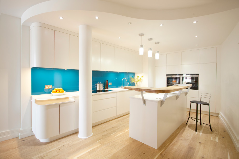 На фото: угловая кухня среднего размера в скандинавском стиле с плоскими фасадами, белыми фасадами, стеклянной столешницей, синим фартуком, фартуком из стекла, светлым паркетным полом и островом с