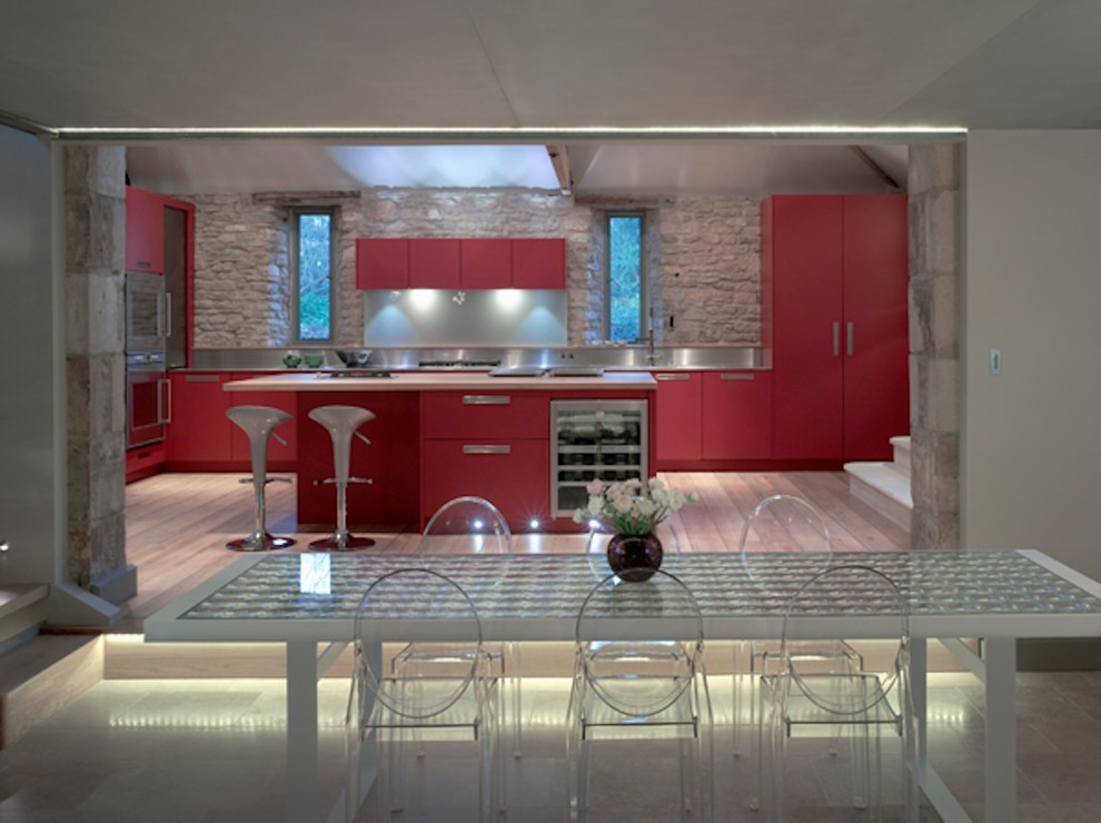 Inspiration for a large contemporary open plan kitchen in London with a submerged sink, flat-panel cabinets, red cabinets, stainless steel worktops, metallic splashback, stainless steel appliances and an island.