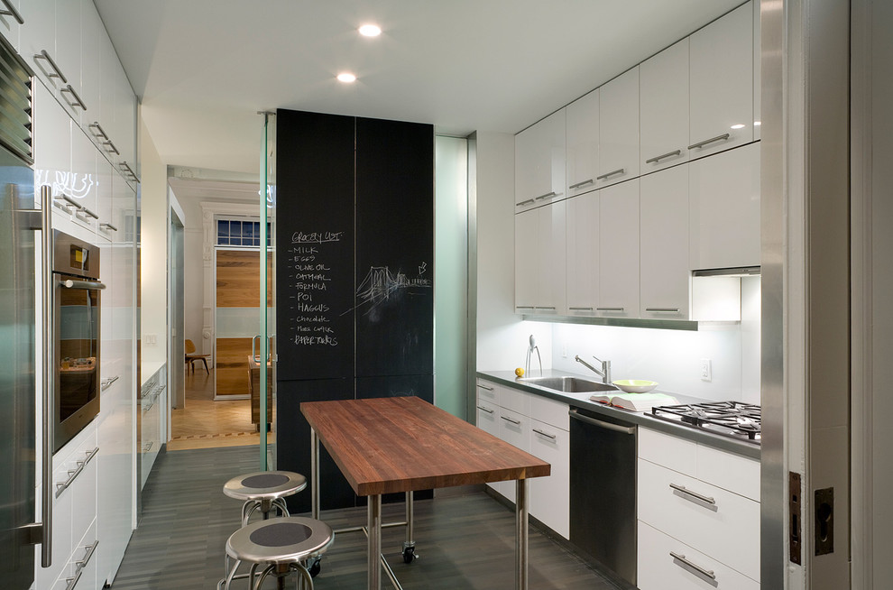 Cette image montre une cuisine vintage fermée avec un placard à porte plane, un électroménager en acier inoxydable, des portes de placard blanches et un évier intégré.