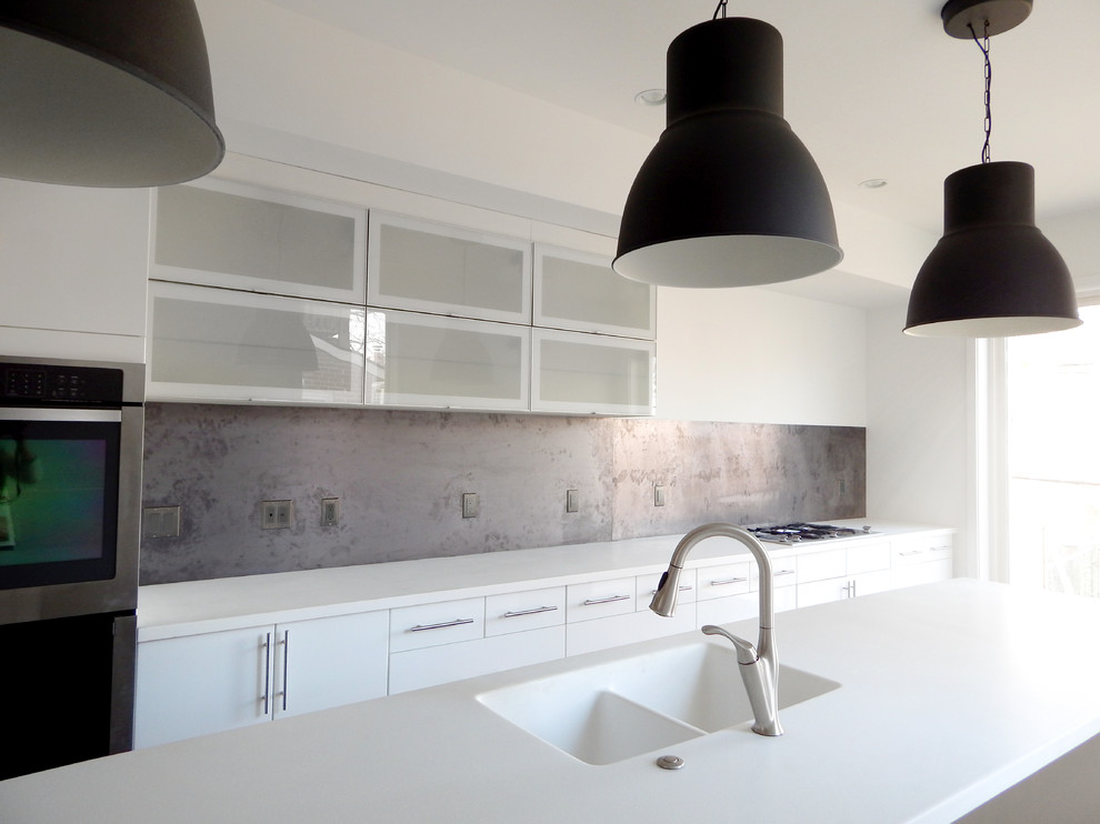 Modern inredning av ett kök, med en integrerad diskho, släta luckor, vita skåp, bänkskiva i kvarts, svart stänkskydd, stänkskydd i metallkakel, rostfria vitvaror och en köksö
