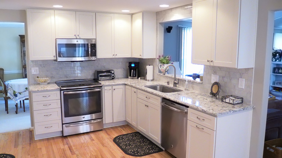 This is an example of a medium sized contemporary l-shaped enclosed kitchen in Baltimore with a single-bowl sink, recessed-panel cabinets, white cabinets, engineered stone countertops, white splashback, porcelain splashback, stainless steel appliances, light hardwood flooring and no island.