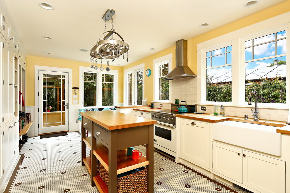 シアトルにある中くらいなヴィクトリアン調のおしゃれなキッチン (エプロンフロントシンク、落し込みパネル扉のキャビネット、白いキャビネット、木材カウンター、白いキッチンパネル、サブウェイタイルのキッチンパネル、シルバーの調理設備、セラミックタイルの床、黄色い床、茶色いキッチンカウンター) の写真