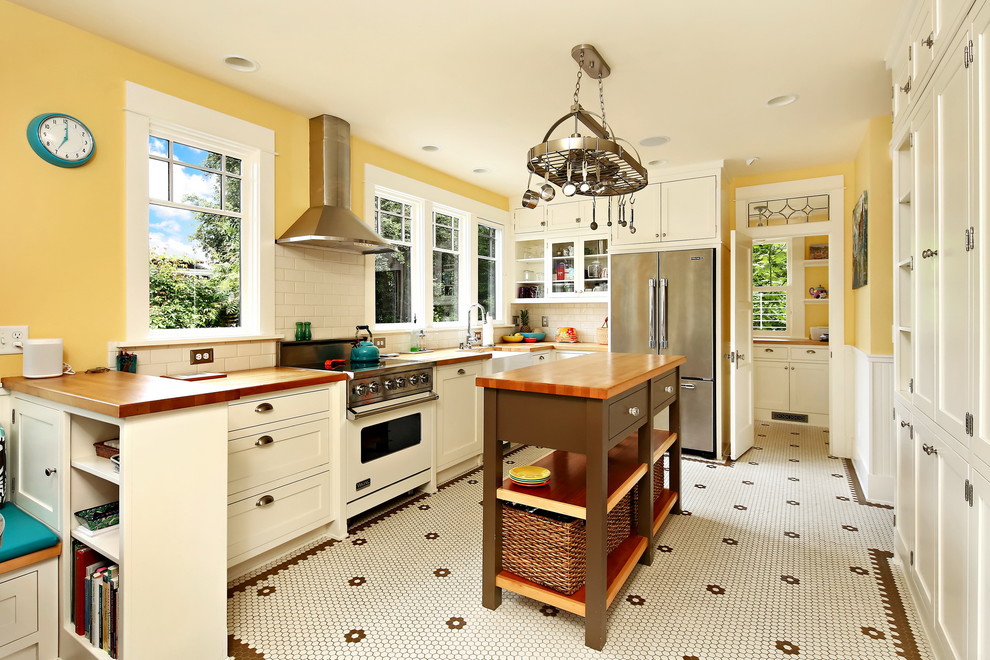Foto på ett mellanstort vintage brun u-kök, med en rustik diskho, skåp i shakerstil, vita skåp, träbänkskiva, vitt stänkskydd, stänkskydd i tunnelbanekakel, rostfria vitvaror, en köksö, flerfärgat golv och klinkergolv i keramik