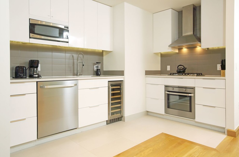 Modern inredning av ett kök, med släta luckor, vita skåp, grått stänkskydd, rostfria vitvaror och beiget golv