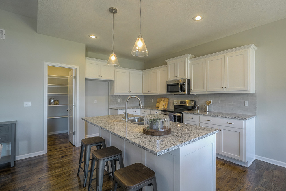 カンザスシティにあるトランジショナルスタイルのおしゃれなキッチン (濃色木目調キャビネット、御影石カウンター、グレーのキッチンパネル、シルバーの調理設備、茶色い床) の写真