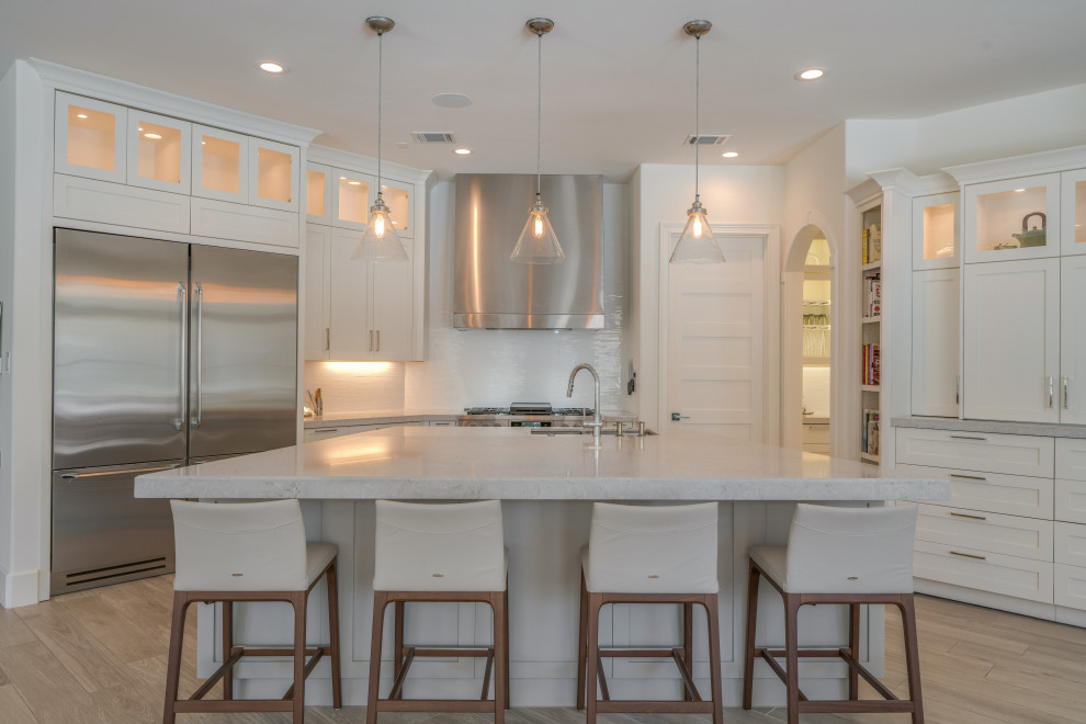 Design ideas for a large classic u-shaped kitchen in Houston with a submerged sink, white cabinets, engineered stone countertops, white splashback, glass tiled splashback, stainless steel appliances, porcelain flooring, an island, beige floors, grey worktops and recessed-panel cabinets.