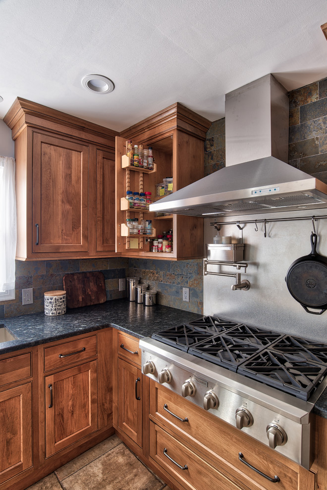Industriell inredning av ett mellanstort kök, med en undermonterad diskho, luckor med profilerade fronter, skåp i mellenmörkt trä, granitbänkskiva, grått stänkskydd, stänkskydd i skiffer, rostfria vitvaror, klinkergolv i keramik, en köksö och brunt golv