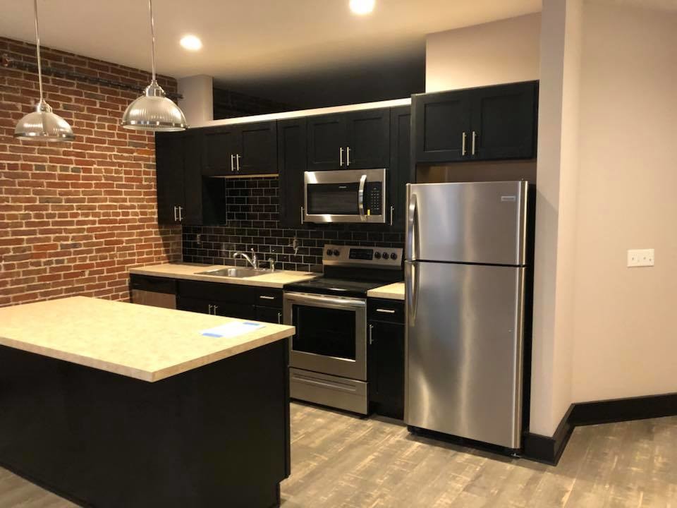Example of a small minimalist single-wall light wood floor and gray floor eat-in kitchen design in Other with a single-bowl sink, shaker cabinets, black cabinets, laminate countertops, black backsplash, subway tile backsplash, stainless steel appliances, an island and white countertops