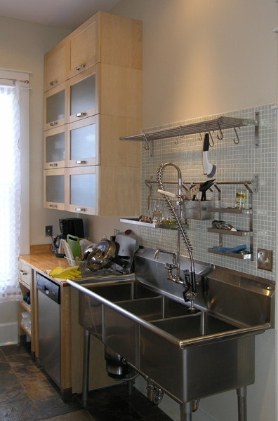 Ejemplo de cocina contemporánea con fregadero de tres senos, puertas de armario de madera clara, salpicadero gris, salpicadero de azulejos de vidrio y electrodomésticos de acero inoxidable