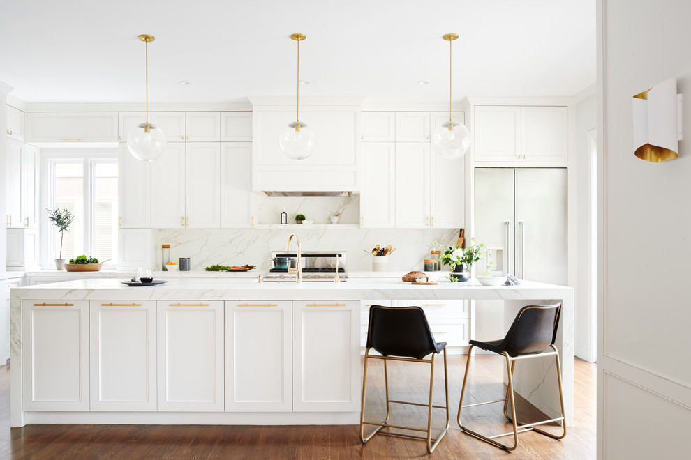 Bild på ett vintage vit vitt l-kök, med luckor med infälld panel, vita skåp, rostfria vitvaror, mellanmörkt trägolv, en köksö och brunt golv
