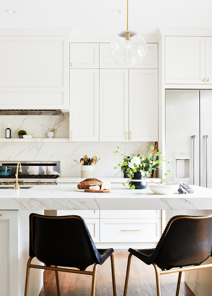 This is an example of a traditional kitchen in San Francisco with recessed-panel cabinets, white cabinets, white splashback, stone slab splashback, stainless steel appliances, medium hardwood flooring, an island and white worktops.