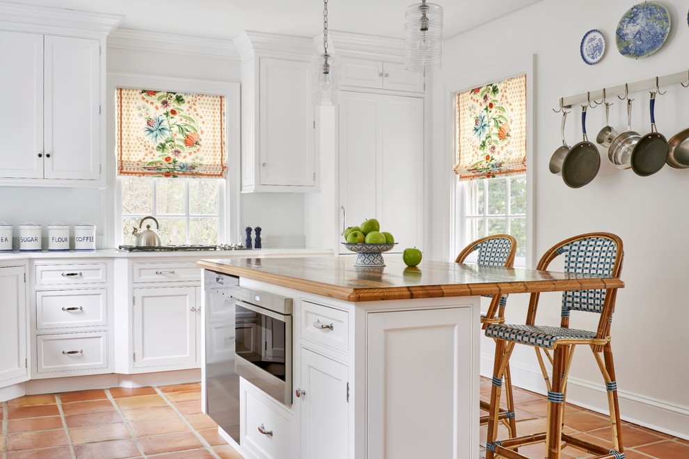 Exempel på ett klassiskt kök, med luckor med profilerade fronter, vita skåp, rostfria vitvaror, klinkergolv i terrakotta och en köksö