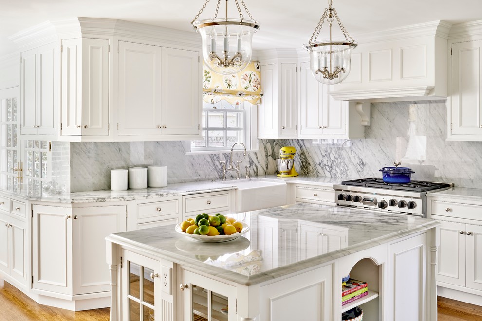 Klassisk inredning av ett kök, med en rustik diskho, luckor med infälld panel, vita skåp, grått stänkskydd, rostfria vitvaror, mellanmörkt trägolv och en köksö
