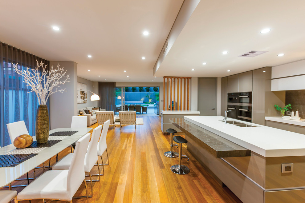 This is an example of a medium sized contemporary galley open plan kitchen in Perth with a built-in sink, flat-panel cabinets, white cabinets, concrete worktops, brown splashback, glass sheet splashback, coloured appliances, light hardwood flooring, an island, brown floors and white worktops.