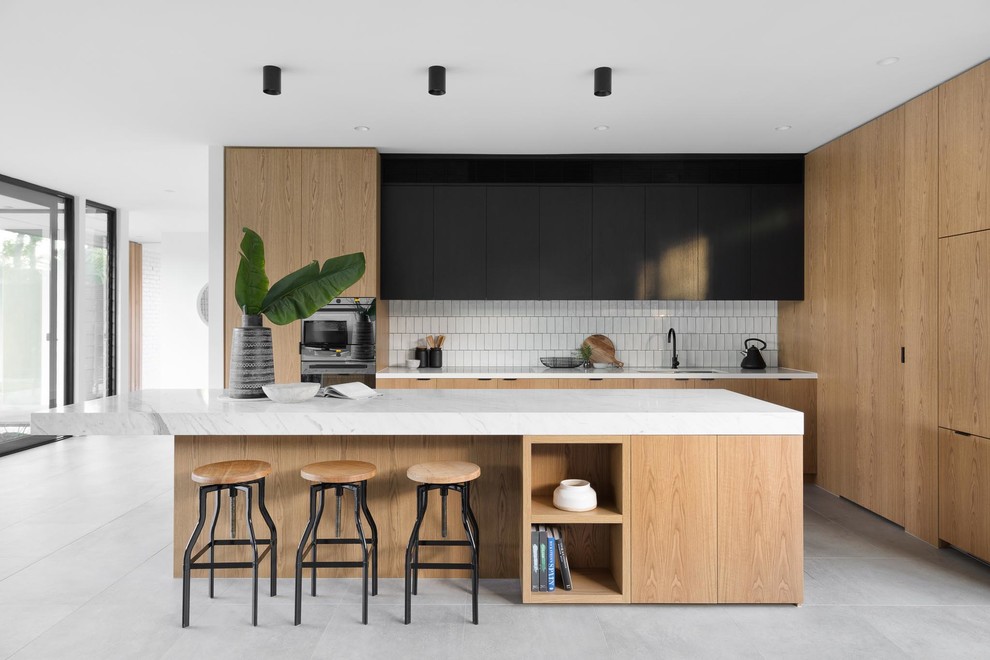 Moderne Küche in L-Form mit Doppelwaschbecken, flächenbündigen Schrankfronten, hellen Holzschränken, Küchenrückwand in Weiß, Kücheninsel, grauem Boden und weißer Arbeitsplatte in Melbourne
