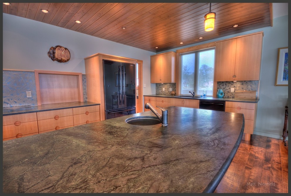 Inspiration for a large contemporary l-shaped open plan kitchen in Vancouver with a submerged sink, flat-panel cabinets, light wood cabinets, soapstone worktops, green splashback, glass sheet splashback, medium hardwood flooring and an island.