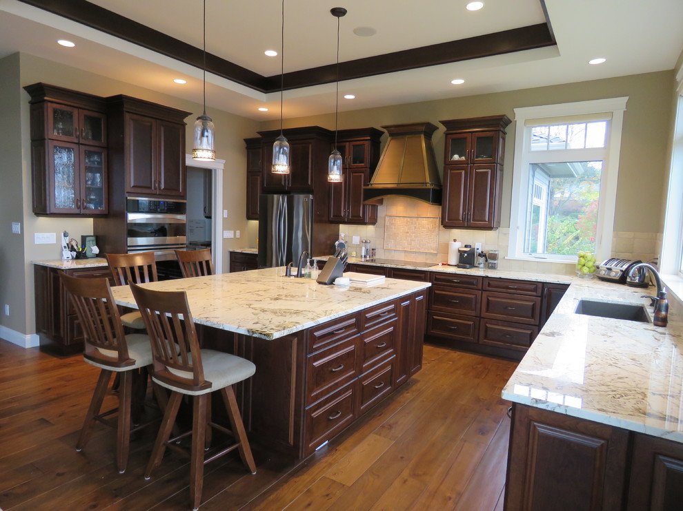 Große Klassische Küche in L-Form mit profilierten Schrankfronten, dunklen Holzschränken, Granit-Arbeitsplatte, Küchenrückwand in Beige, Rückwand aus Keramikfliesen, Küchengeräten aus Edelstahl, braunem Holzboden und Kücheninsel in Vancouver