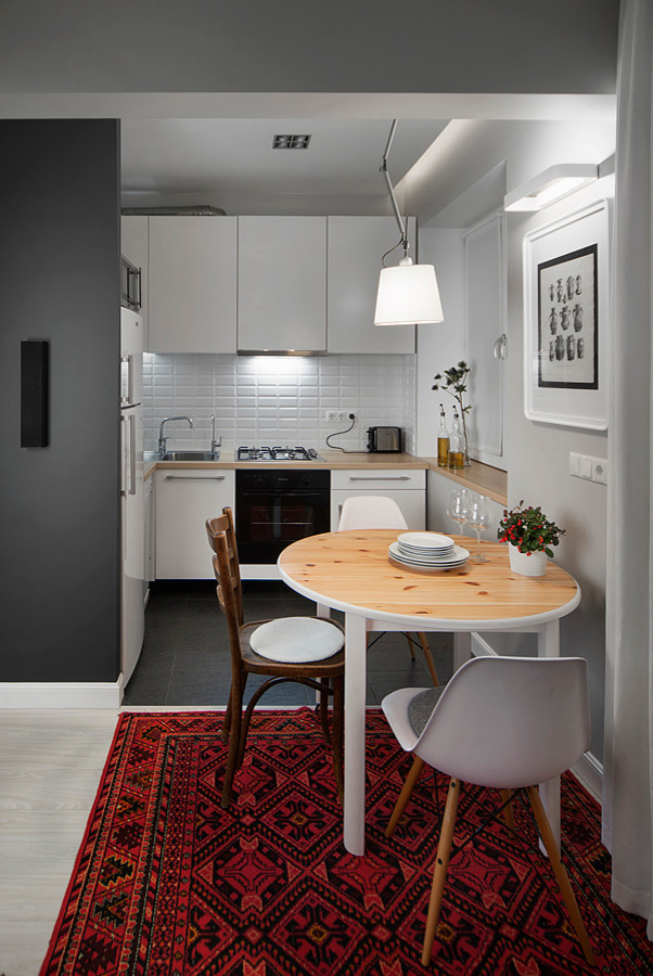 На фото: угловая кухня-гостиная в современном стиле с накладной мойкой, плоскими фасадами, белыми фасадами, деревянной столешницей, белым фартуком, фартуком из плитки кабанчик и черной техникой без острова