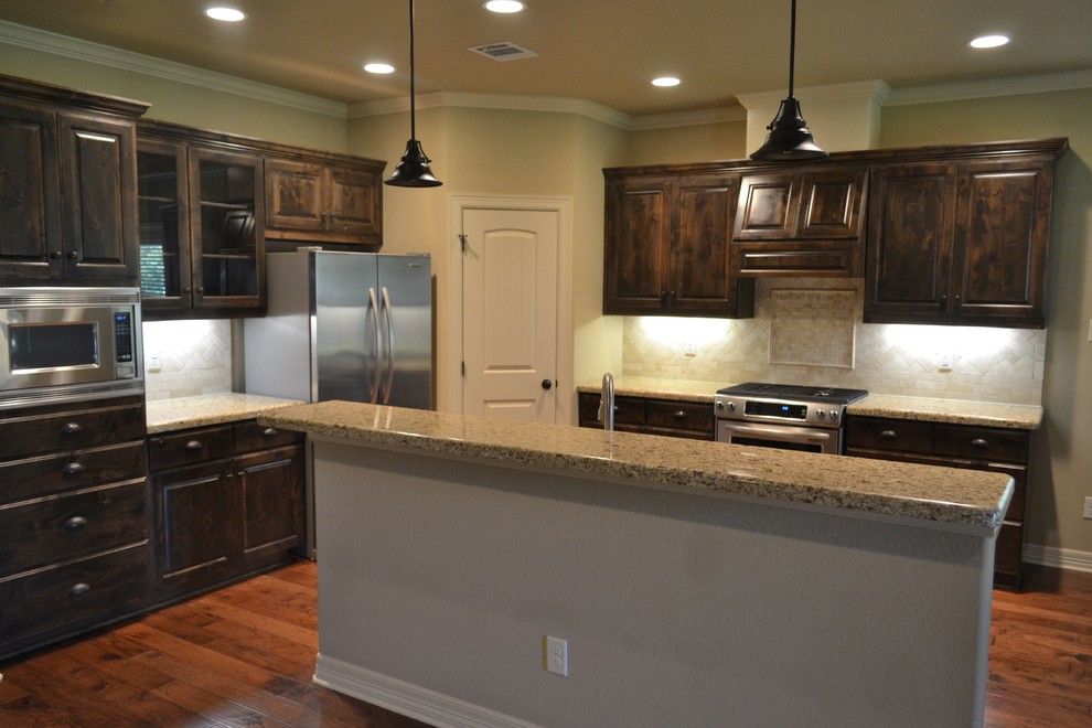 Offene Rustikale Küche mit profilierten Schrankfronten, dunklen Holzschränken, Granit-Arbeitsplatte, braunem Holzboden und Kücheninsel in Austin
