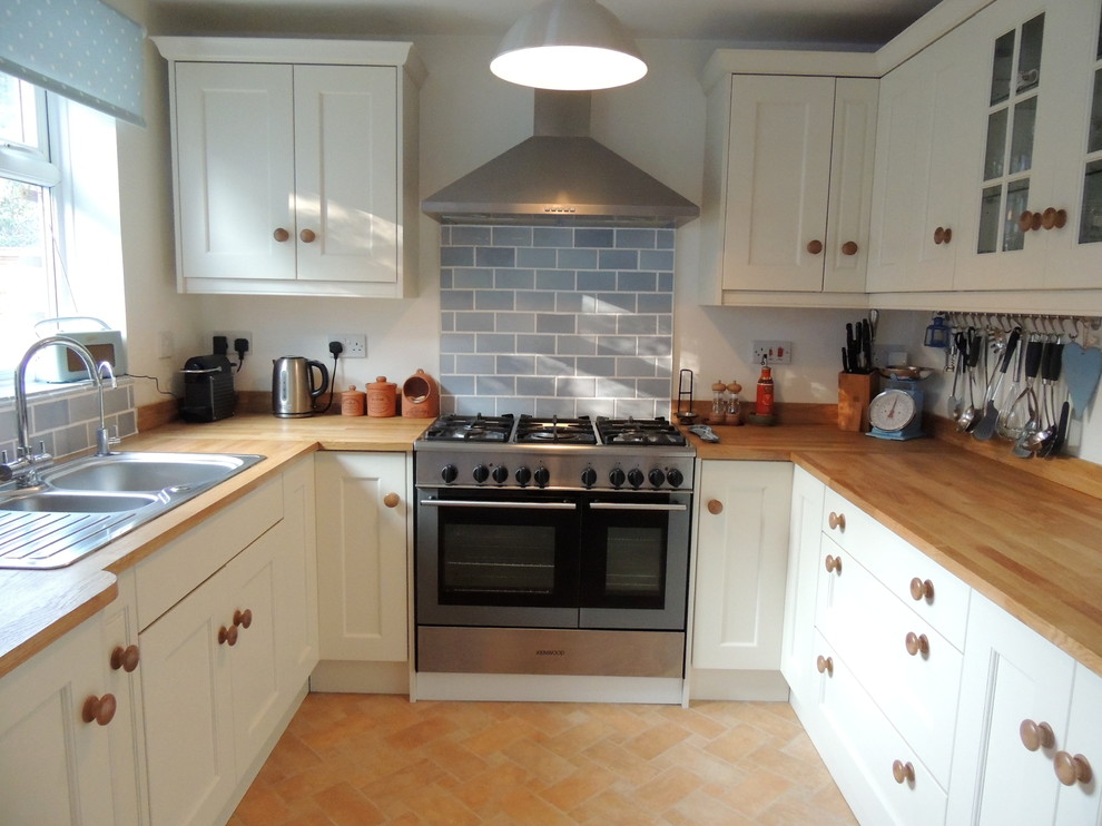 Foto på ett litet lantligt kök, med en nedsänkt diskho, skåp i shakerstil, träbänkskiva, grått stänkskydd, stänkskydd i tunnelbanekakel och rostfria vitvaror