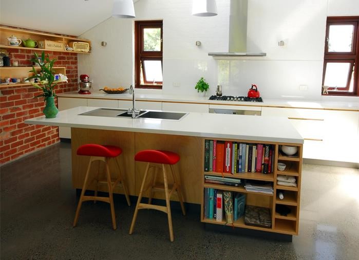 Modern inredning av ett mellanstort vit vitt kök, med en dubbel diskho, luckor med infälld panel, skåp i ljust trä, bänkskiva i kvarts, vitt stänkskydd, glaspanel som stänkskydd, rostfria vitvaror, betonggolv, en köksö och brunt golv