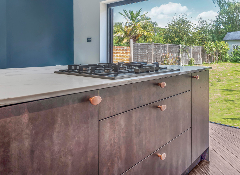 Photo of an industrial single-wall kitchen in Berkshire with shaker cabinets, blue cabinets, brick splashback, black appliances, an island and brown floors.