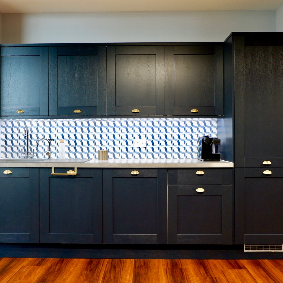 Photo of a small contemporary single-wall open plan kitchen in Manchester with a built-in sink, recessed-panel cabinets, blue cabinets, laminate countertops, blue splashback, cement tile splashback, integrated appliances, laminate floors, no island, brown floors and grey worktops.