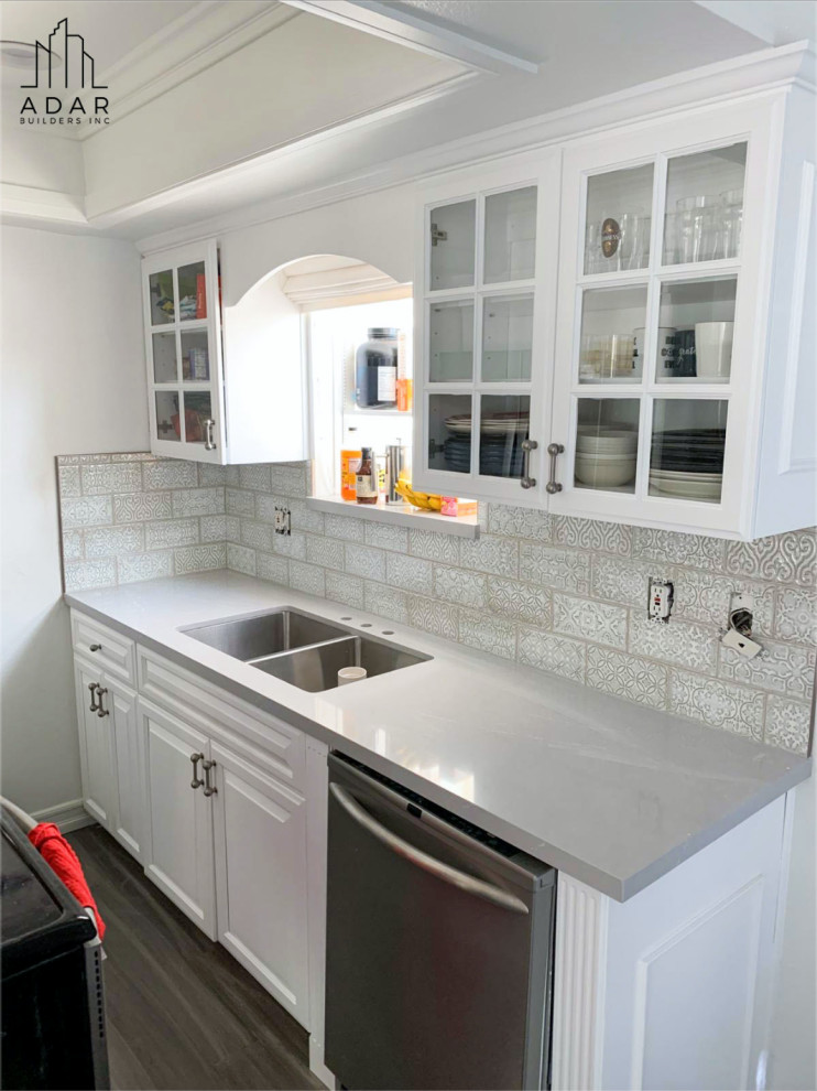 Inspiration för små moderna grått kök, med luckor med upphöjd panel, vita skåp, marmorbänkskiva, vitt stänkskydd, rostfria vitvaror, mellanmörkt trägolv, en köksö och brunt golv