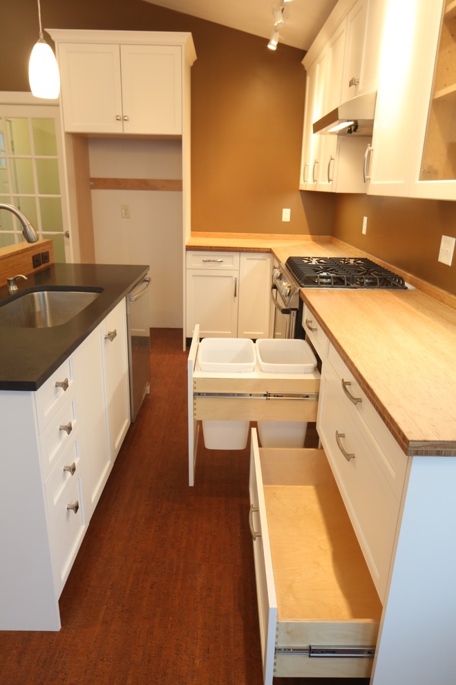 Inspiration for a small contemporary galley cork floor eat-in kitchen remodel in Philadelphia with an undermount sink, recessed-panel cabinets, white cabinets, wood countertops, brown backsplash and stainless steel appliances