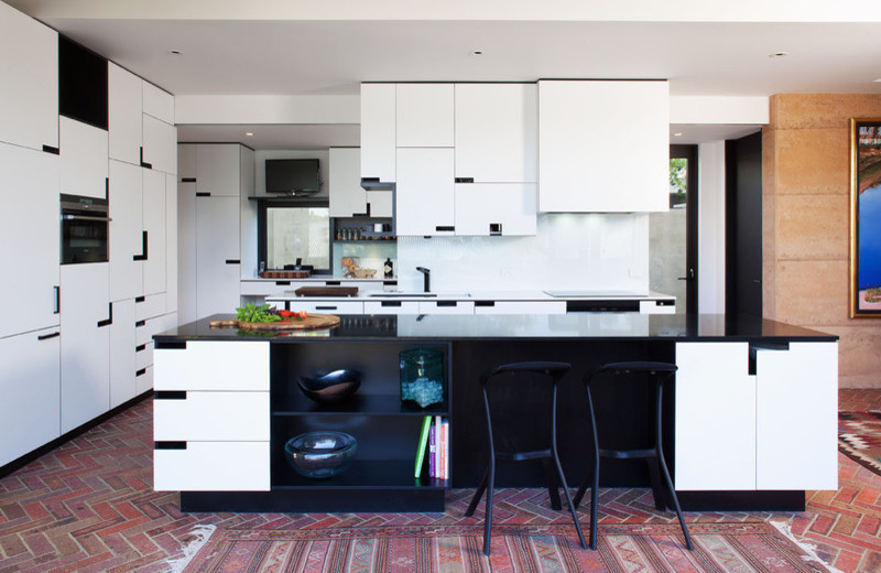 Exempel på ett modernt kök, med en nedsänkt diskho, släta luckor, vita skåp, granitbänkskiva, vitt stänkskydd, glaspanel som stänkskydd, svarta vitvaror, tegelgolv och en köksö