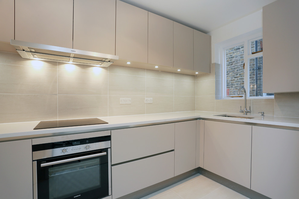 Ejemplo de cocinas en U minimalista pequeño cerrado con puertas de armario beige y electrodomésticos de acero inoxidable