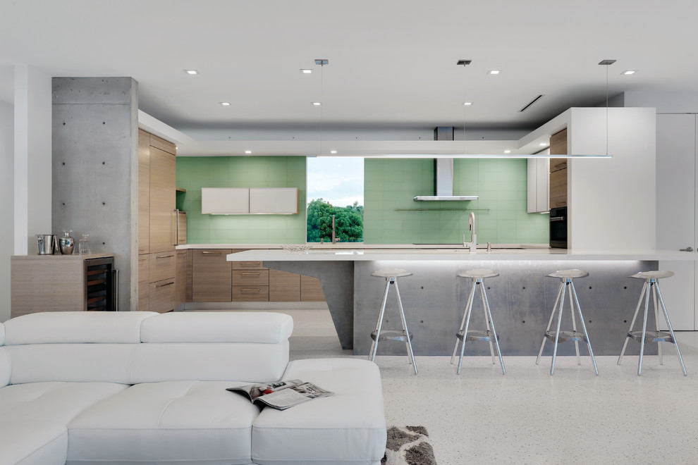 タンパにある高級な広いコンテンポラリースタイルのおしゃれなキッチン (アンダーカウンターシンク、フラットパネル扉のキャビネット、淡色木目調キャビネット、珪岩カウンター、緑のキッチンパネル、ガラスタイルのキッチンパネル、パネルと同色の調理設備、コンクリートの床、白い床、白いキッチンカウンター) の写真
