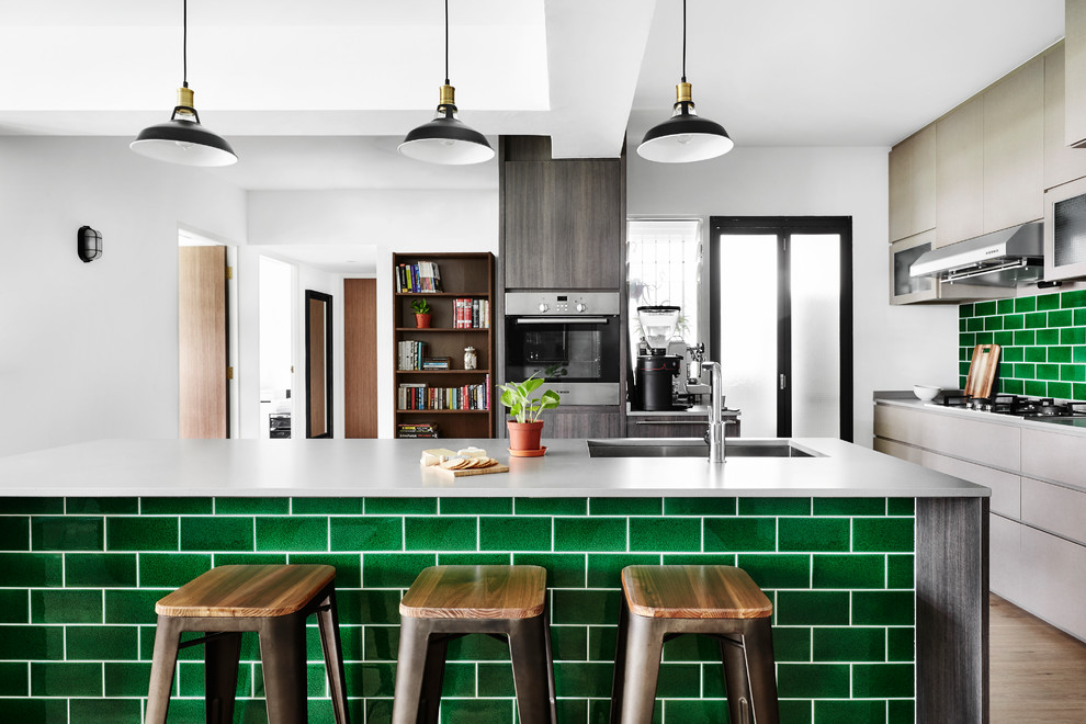 Moderne Küche mit Unterbauwaschbecken, flächenbündigen Schrankfronten, beigen Schränken, Küchenrückwand in Grün, Rückwand aus Metrofliesen, Küchengeräten aus Edelstahl, hellem Holzboden, Kücheninsel und grauer Arbeitsplatte in Singapur
