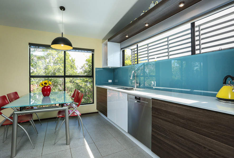 Bild på ett mellanstort funkis kök, med blått stänkskydd, glaspanel som stänkskydd, rostfria vitvaror, vitt golv, en dubbel diskho, släta luckor, vita skåp, bänkskiva i kvarts, klinkergolv i keramik och en halv köksö