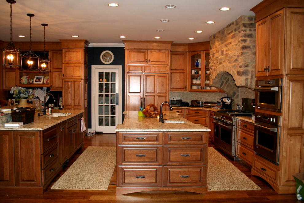 Inspiration for a mid-sized timeless u-shaped dark wood floor eat-in kitchen remodel in Raleigh with an undermount sink, raised-panel cabinets, medium tone wood cabinets, granite countertops, gray backsplash, stone tile backsplash, stainless steel appliances and two islands