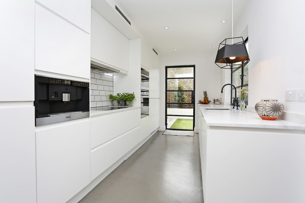 Small industrial galley enclosed kitchen in London with flat-panel cabinets, white cabinets, white splashback, metro tiled splashback, concrete flooring, no island and grey floors.
